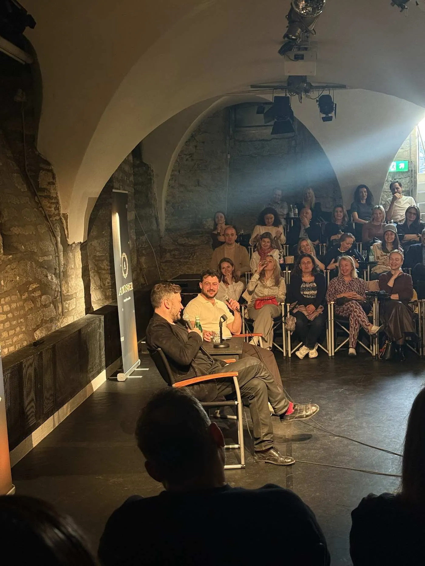 A vaulted stone cellar during a conversation with a guest and a full audience